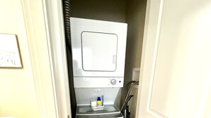 A compact laundry room with a washing machine and dryer, a small basket, and a hose.