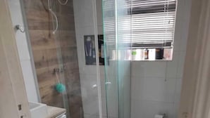 A bathroom with a glass shower enclosure, a toilet, and a sink. - Banesha Hostel (São Paulo)