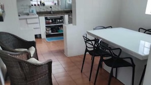 A compact kitchen with a central island, a dining area with chairs, and a wicker sofa. - Banesha Hostel (São Paulo)