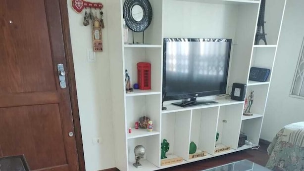 A living room with a wooden floor, a glass coffee table, a television on a white entertainment unit, and a fish tank. - Banesha Hostel (São Paulo)