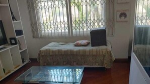 A room with a bed, a glass coffee table, a TV on a shelf, and a window with bars. - Banesha Hostel (São Paulo)