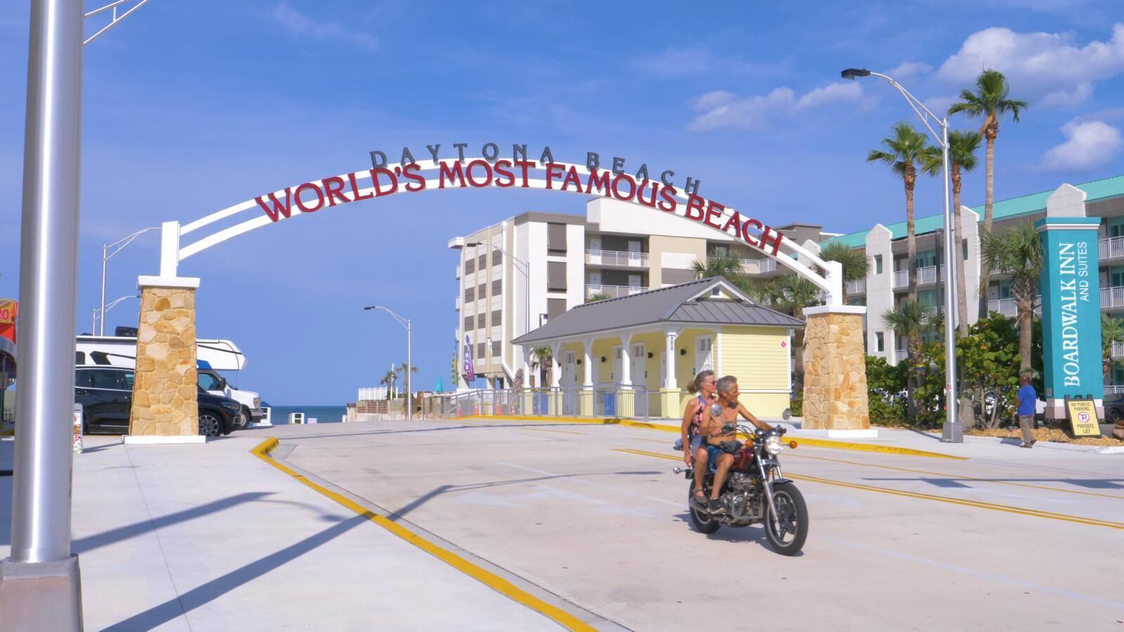 Una veduta della strada con un cartello che recita 'Daytona Beach Spiaggia più famosa del mondo' e un edificio con l'insegna 'Boardwalk Suites'.