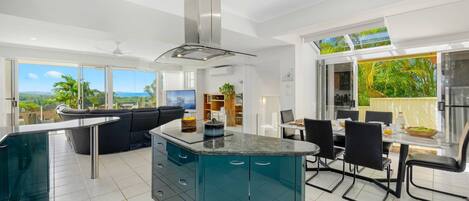 Una cocina moderna con una isla central, un área de comedor con mesa y sillas, y un ventanal que ofrece vistas al exterior.