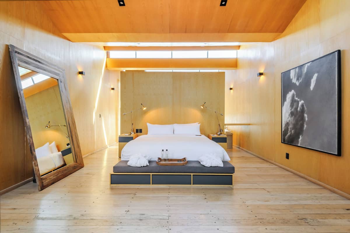 Quarto moderno com cama grande, mesas de cabeceira, espelho e uma obra de arte emoldurada na parede.