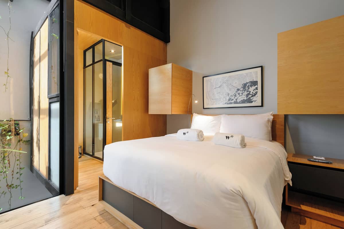 Quarto de hotel moderno com uma cama grande, lambris de madeira, uma obra de arte emoldurada na parede e uma mesinha de cabeceira com controle remoto.