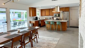 Una cocina moderna con armarios de madera, una isla central con taburetes de bar, un comedor con mesa y sillas, y vistas al exterior.