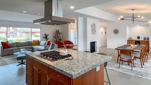 Una cocina moderna con una isla central, un comedor con mesa y sillas de madera, y una sala de estar con sofá y sillones.