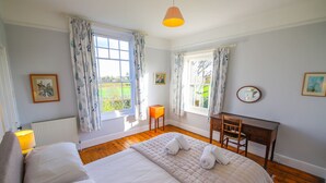 A bedroom with a large bed, two windows with curtains, a desk, and a chair.