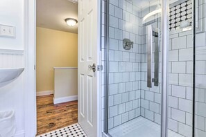 Un baño con cabina de ducha de vidrio, paredes cubiertas de azulejos blancos y suelo de madera.