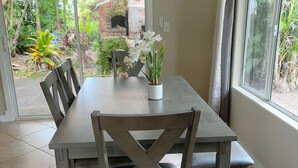 A dining area with a table and chairs, a potted plant, and a view through a glass door to an outdoor garden. - 3 bedroom 2 bath Orchid house in Paradise (Hawaiian Paradise Park)