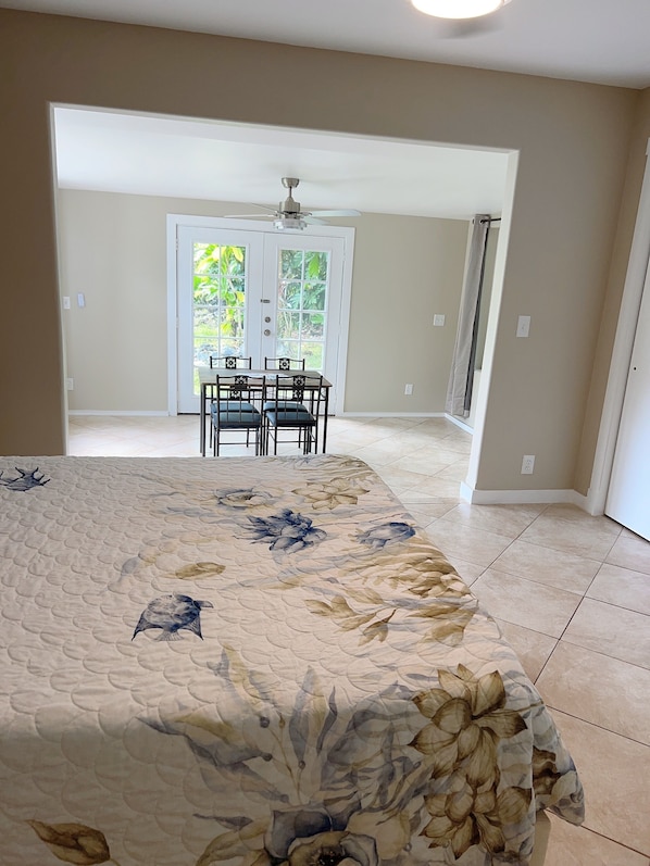 A bedroom with a floral bedspread, a dining area with a table and chairs, and a view of a garden through a glass door.