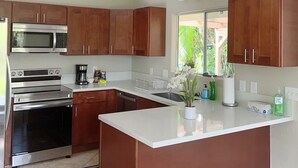 A modern kitchen with wooden cabinets, stainless steel appliances, and a large island. - 3 bedroom 2 bath Orchid house in Paradise (Hawaiian Paradise Park)