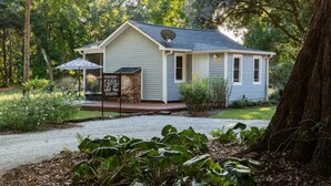 Une maison de plain-pied avec une antenne parabolique, une véranda avec une table et un parasol, et un jardin où poussent différentes plantes.