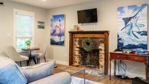 Un salon avec une cheminée, un téléviseur fixé au-dessus et un tableau représentant un poisson au mur.