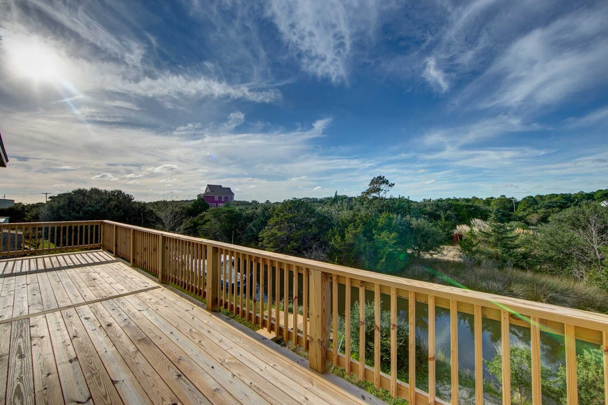 A wooden deck with a railing overlooking a forested area and a distant house.