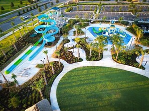 Vue aérienne d’un parc aquatique avec un grand toboggan en spirale, une zone de piscines et des aménagements paysagers environnants.