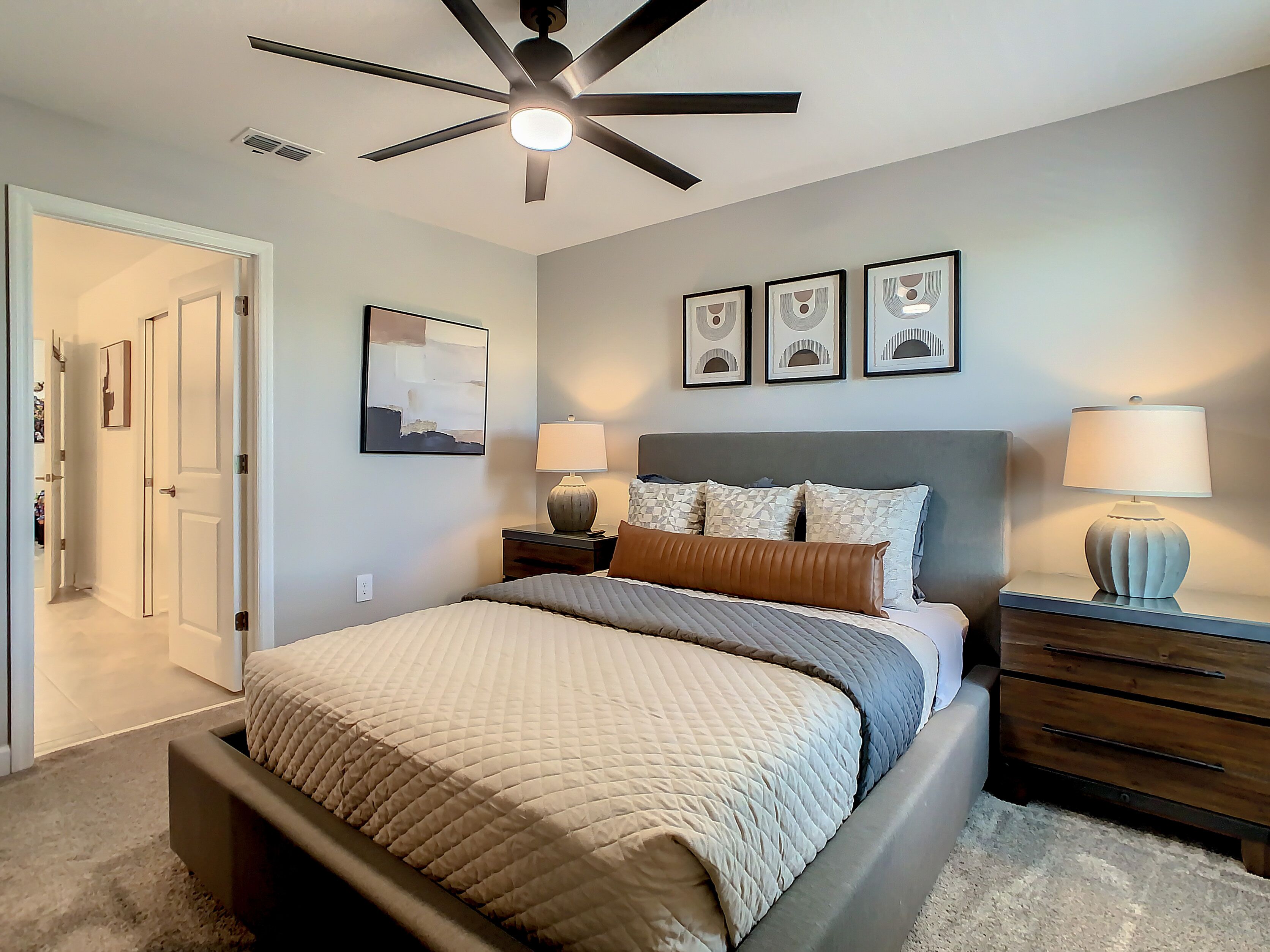 A bedroom with a bed, bedside tables, a ceiling fan, and a door leading to another room.