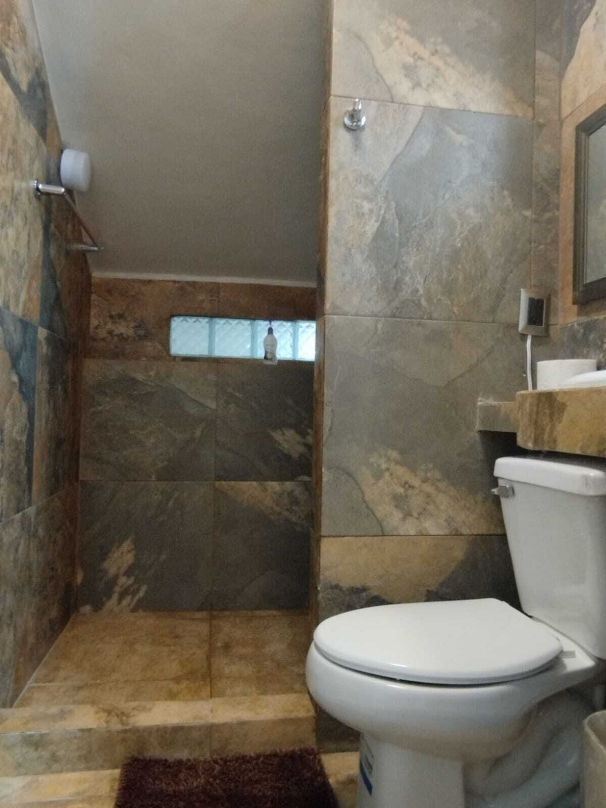 Een badkamer met een douche, toilet en marmeren wanden.