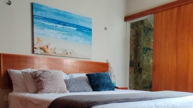 A bedroom with a wooden headboard, a large bed with white bedding, and a painting of a beach scene on the wall. - Charming villa in Tulum, near the Tulum Ruins. (Tulum)