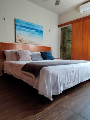Ein Schlafzimmer mit Holzfußende, einem großen Bett mit weißer Bettwäsche und einem Bild einer Strandansicht an der Wand.