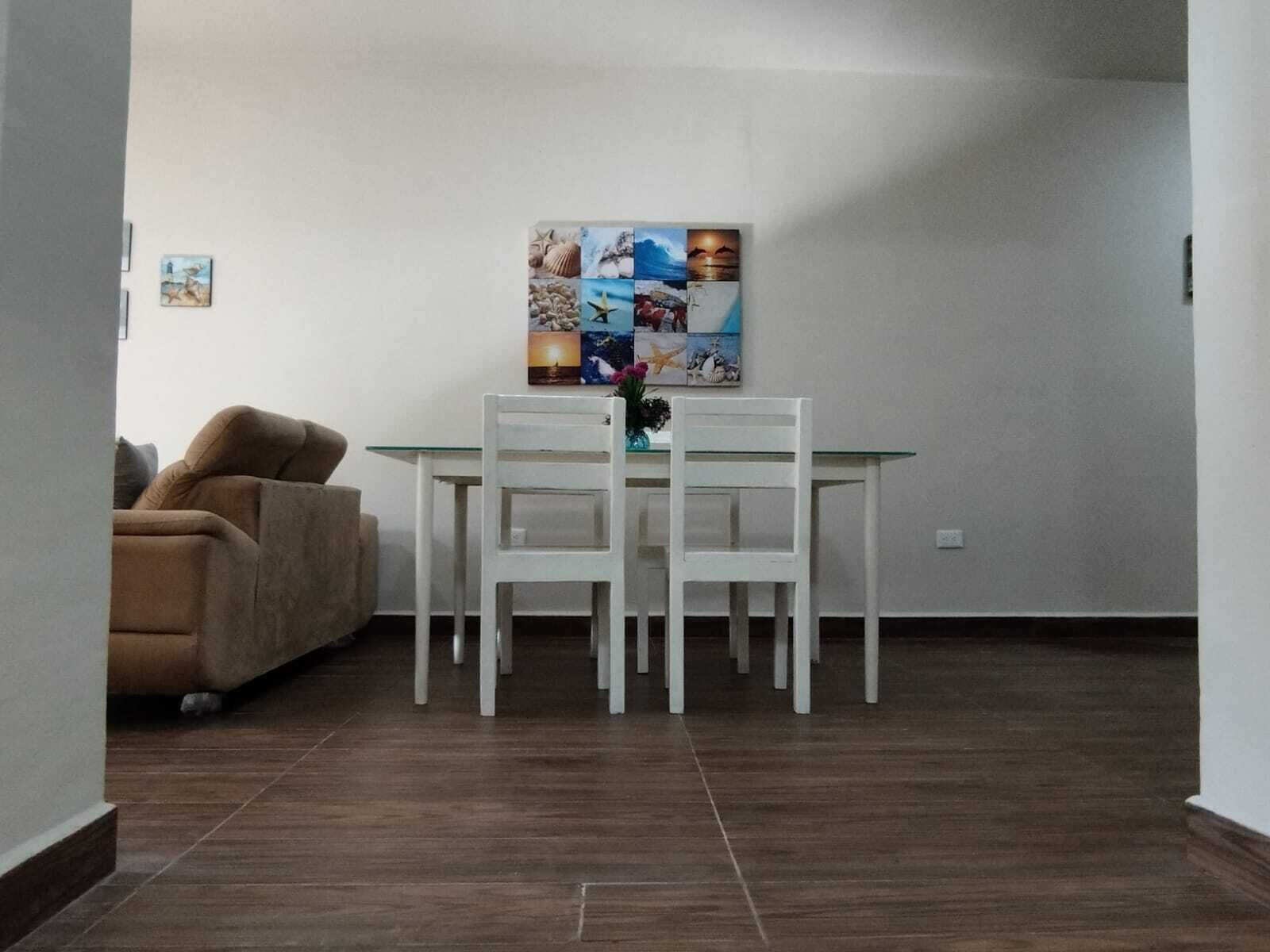 A dining area with a white table and chairs, a beige sofa, and a wall-mounted artwork.