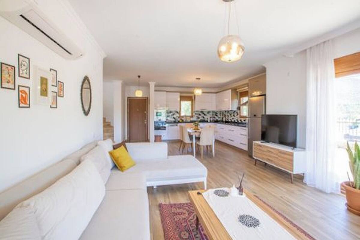 A modern living room with a sofa, a dining area, and a kitchen in the background.