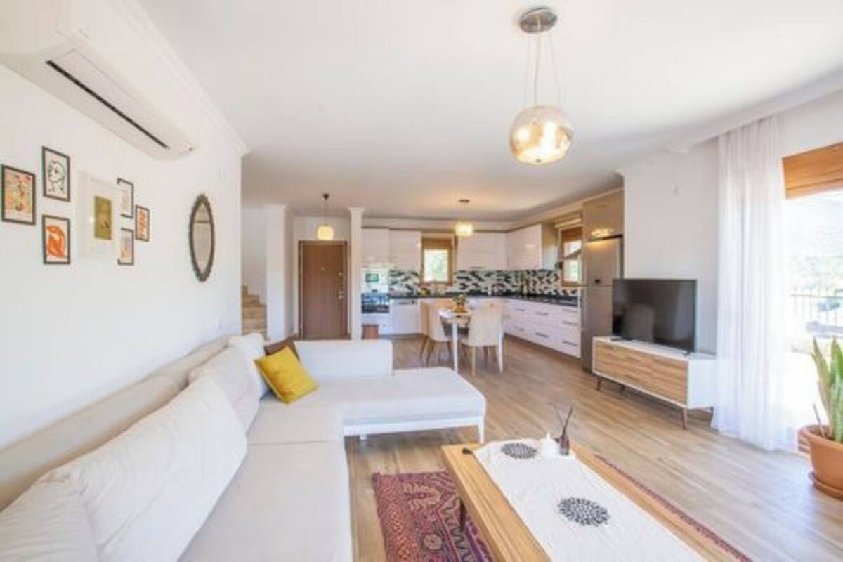 A modern living room with a sofa, a dining table, and a kitchen in the background.