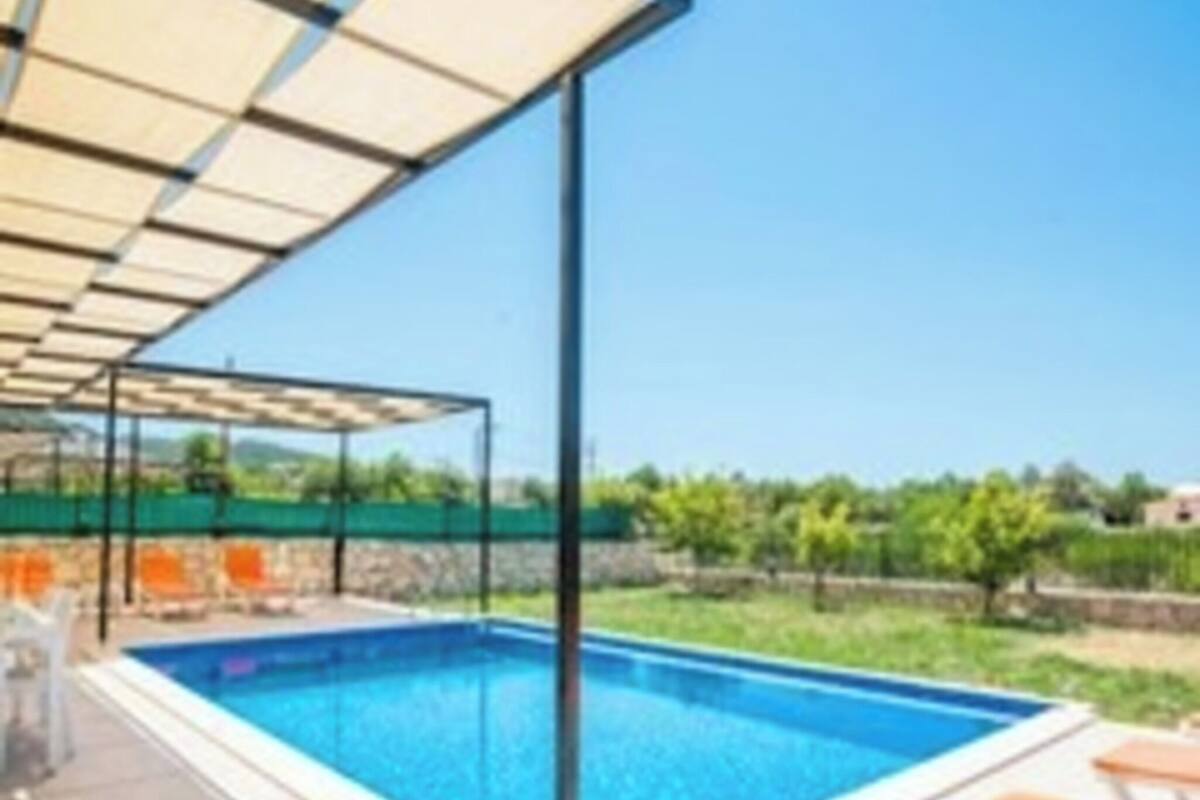A swimming pool with a pergola overhead, surrounded by a tiled deck and a view of greenery.