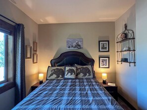 Une chambre à coucher avec un grand lit, deux lampes de chevet, une tête de lit ornée d’une œuvre d’art sur le thème des ours et une fenêtre avec des rideaux.