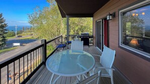 A covered outdoor area with a glass table and chairs, a grill, and a view of a road and trees. - Lakeview Getaway-Walk To Downtown Bigfork, Rated #1 Lake town in USA (Bigfork)