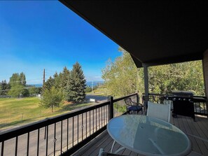 Un balcon avec une table et des chaises en verre, donnant sur un espace verdoyant et des arbres.