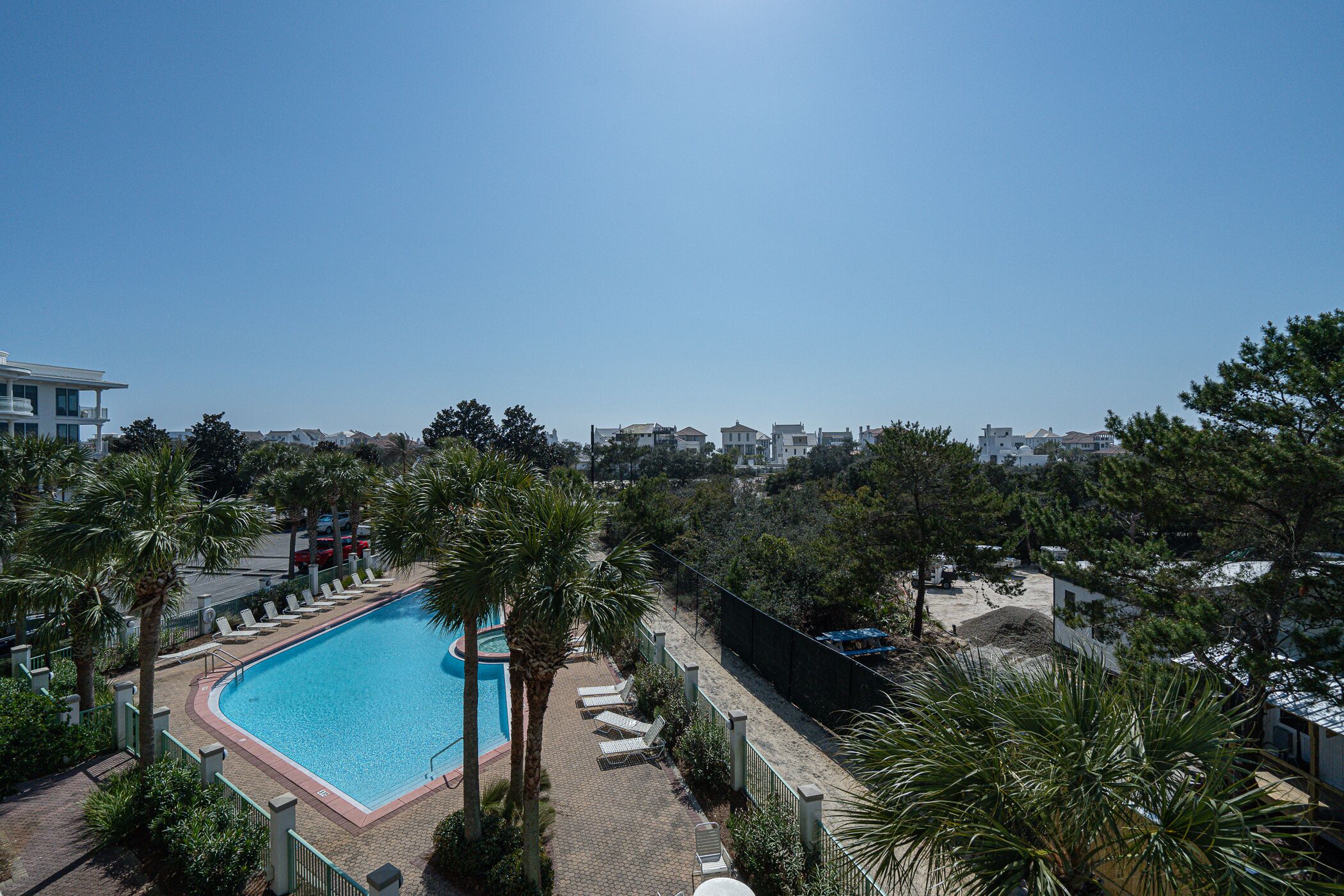 A rectangular swimming pool with a surrounding deck, palm trees, and a view of residential buildings in the background.