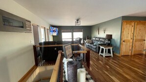 Een ruime woonkamer met een houten vloer, een zwarte leren bank, een witte salontafel en een aan de muur bevestigde televisie.