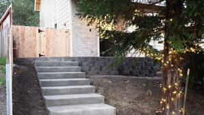 A concrete staircase leading up to a house with a wooden fence and a tree with string lights.