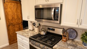 A kitchen with white cabinets, a stainless steel stove, a microwave, and a wooden door.
