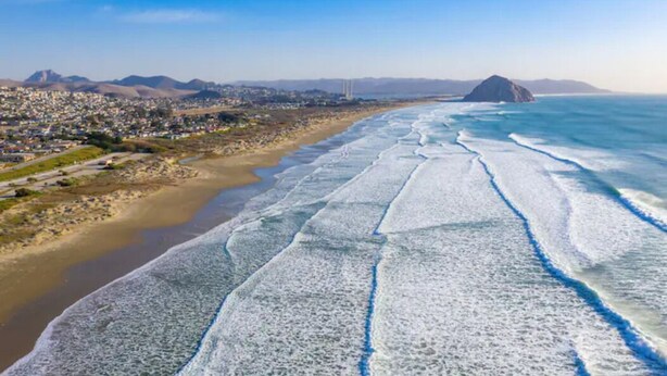 A coastal cityscape with a beach, mountains, and a clear sky.