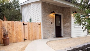 A house with a brick exterior, a wooden fence, and a concrete pathway leading to the door.