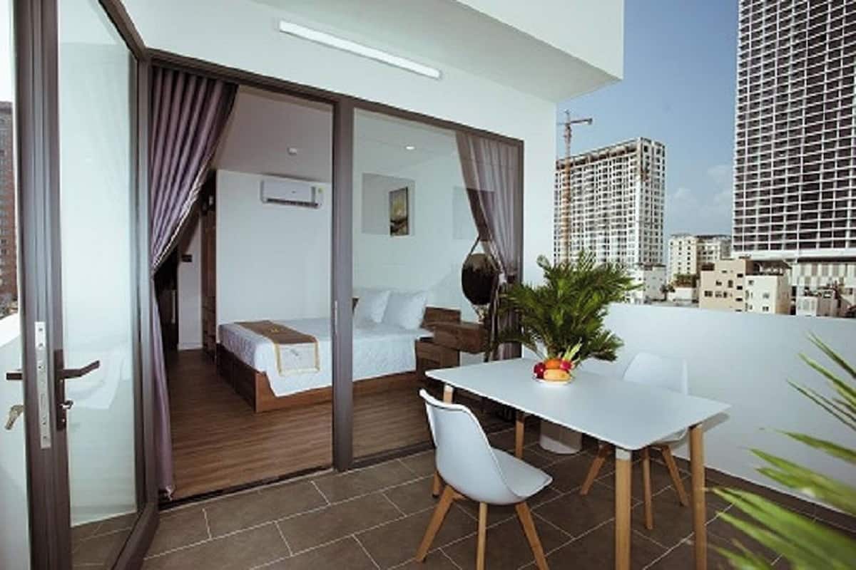A modern hotel room with a balcony, a bed, a desk, and a dining area.