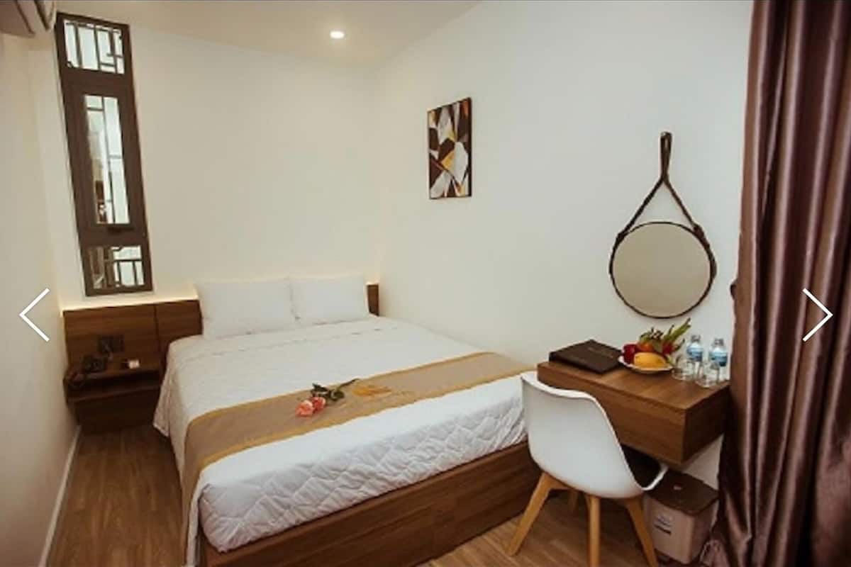 Une chambre d’hôtel avec un lit, un bureau et une chaise, un miroir rond et une fenêtre avec des rideaux.