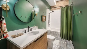 Un baño moderno con pared verde, un espejo redondo, un lavamanos blanco y una zona de ducha.