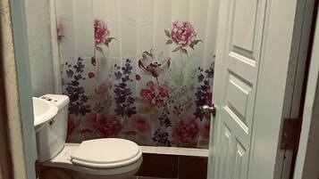 Un baño con inodoro, lavamanos y cortina de ducha estampada con motivos florales.