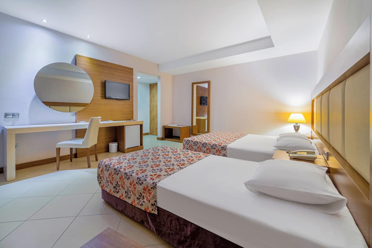 Une chambre d’hôtel avec deux lits, un bureau, une chaise, une télévision et une lampe.