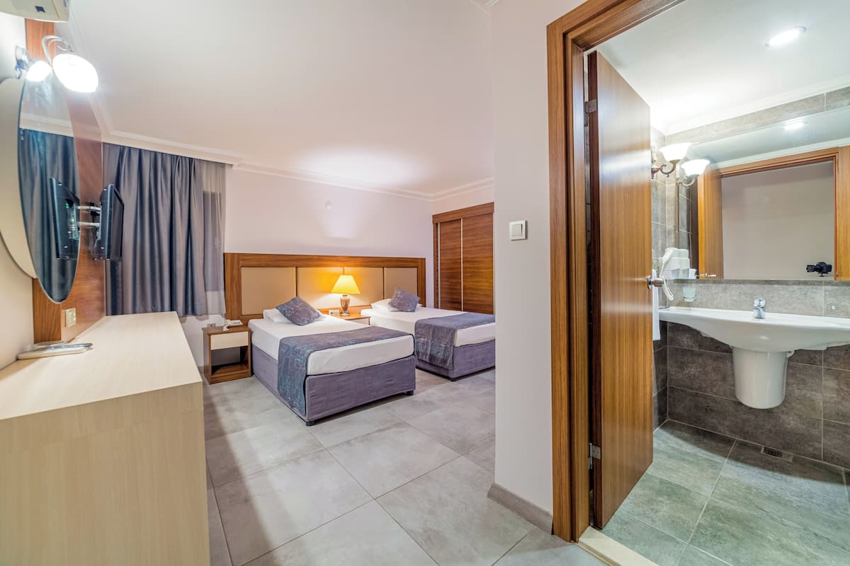Une chambre d’hôtel avec deux lits, un bureau, une lampe, un miroir et une salle de bain équipée d’un lavabo et d’un miroir.