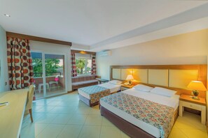 A hotel room with two beds, a balcony, a dining area, and a view of greenery. - Justiniano Club Alanya (Alanya)