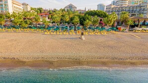 A beach with clear water, yellow lounge chairs, and palm trees. - Justiniano Club Alanya (Alanya)