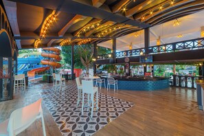 An indoor area with a pool slide, seating, and a bar area. - Justiniano Club Alanya (Alanya)