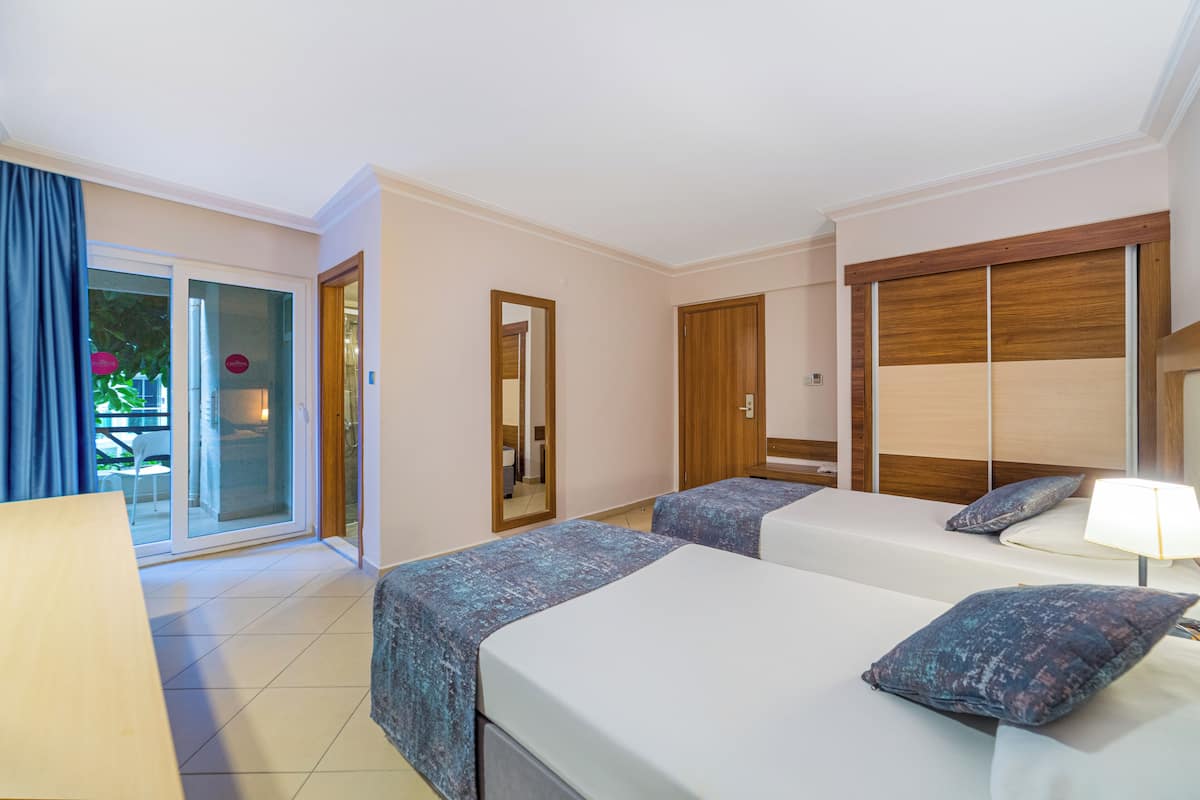 Une chambre d’hôtel avec deux lits, une porte coulissante donnant sur le balcon et une armoire en bois.