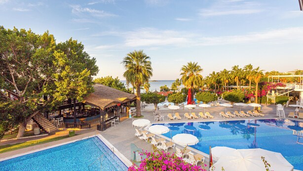 A pool area with lounge chairs and umbrellas, a bar, and a view of the sea. - Justiniano Club Alanya (Alanya)