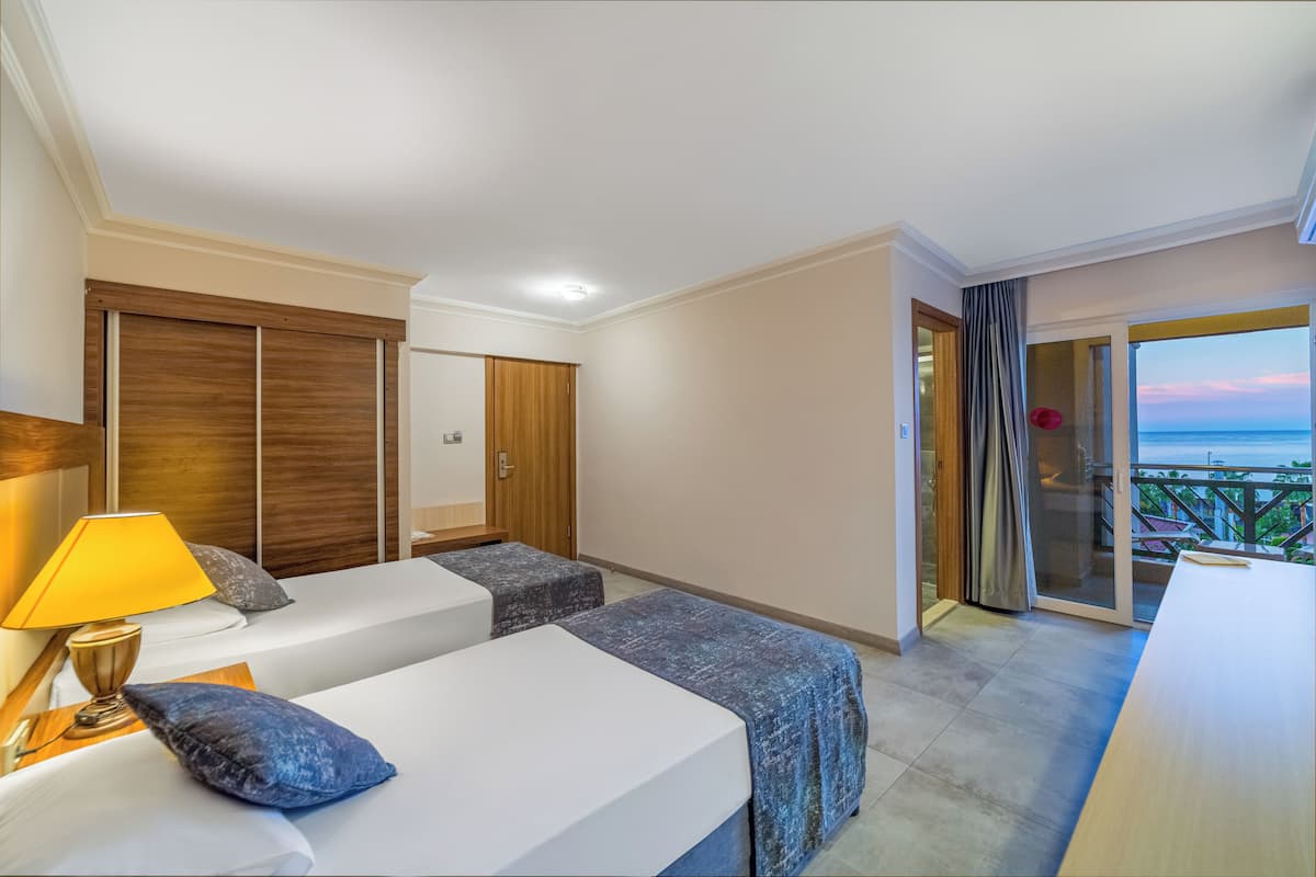 Une chambre d’hôtel avec deux lits, une armoire en bois, un balcon avec vue sur la mer et une table.