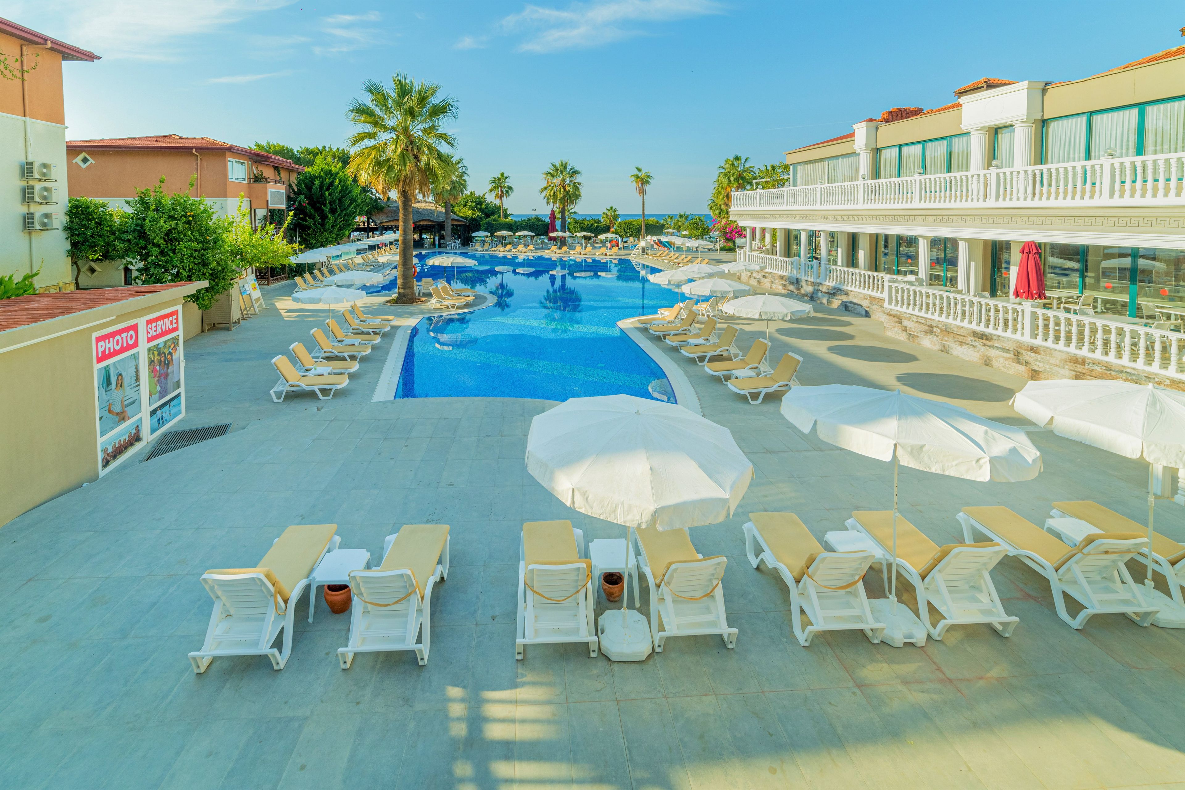 A pool area with sun loungers, umbrellas, and a building with a balcony.